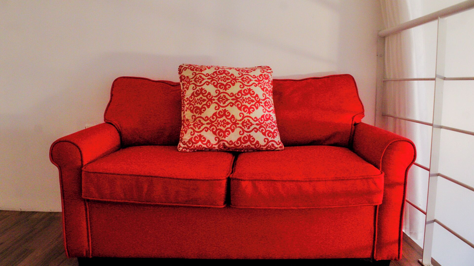 A red sofa with a patterned pillow against a white wall.