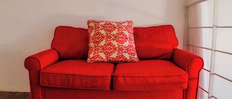 A red sofa with a patterned pillow against a white wall.
