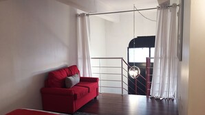 Una camera da letto moderna con un divano rosso, un letto, un tappeto nero e una scala che conduce a un piano superiore.