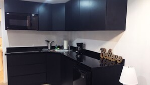 Una cucina moderna con mobili scuri, forno a microonde integrato e macchina del caffè.