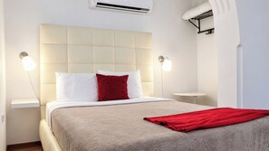 A hotel room with a bed, a bedside table, a wall-mounted air conditioner, and a wall-mounted light fixture.