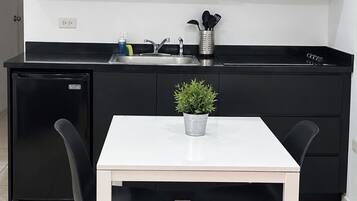 A modern kitchen with black cabinets, a white countertop, a black refrigerator, a microwave, and a small potted plant on the table.