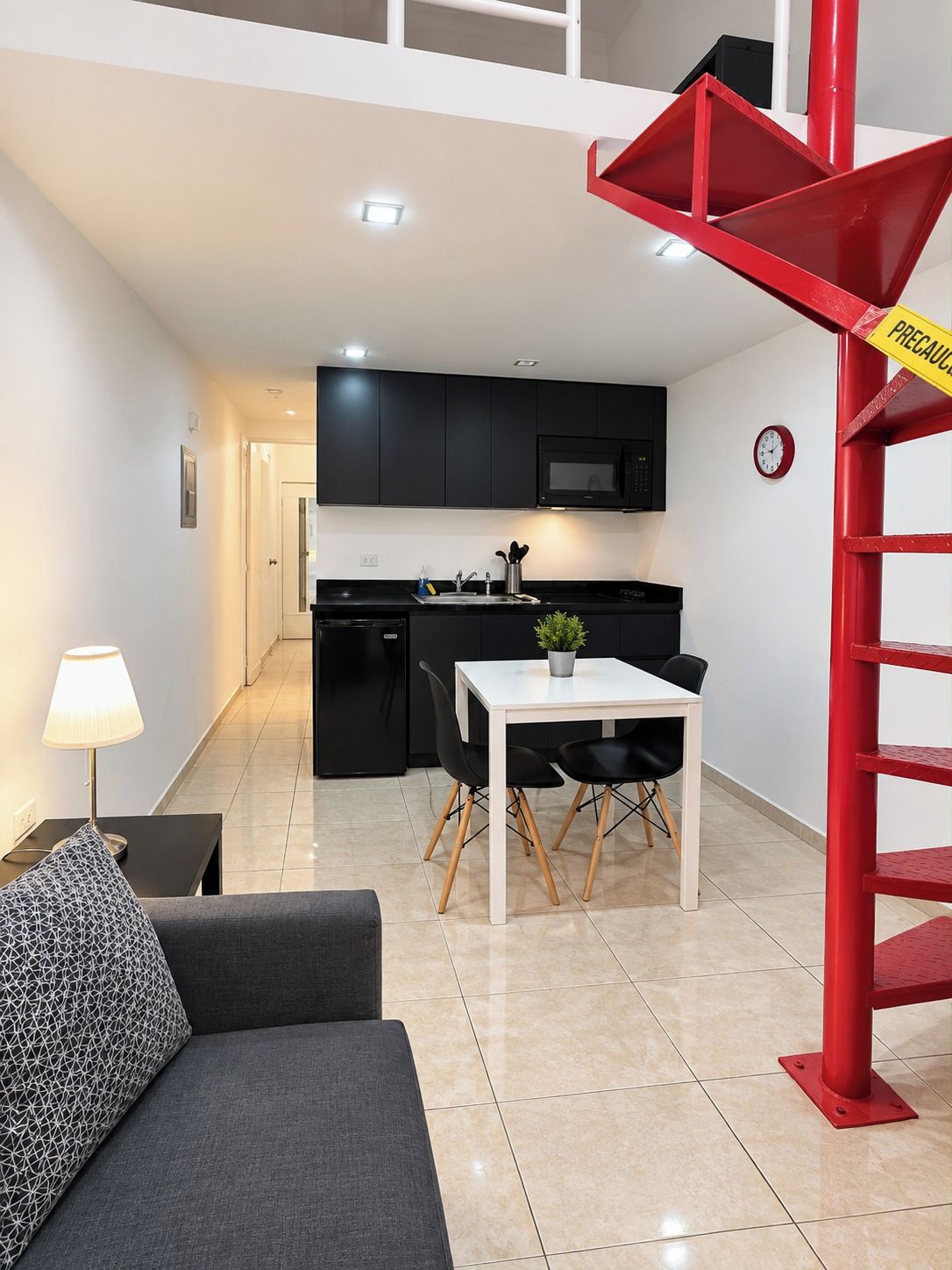 Een modern appartement met een eethoek, kitchenette en een rode spiltrap.