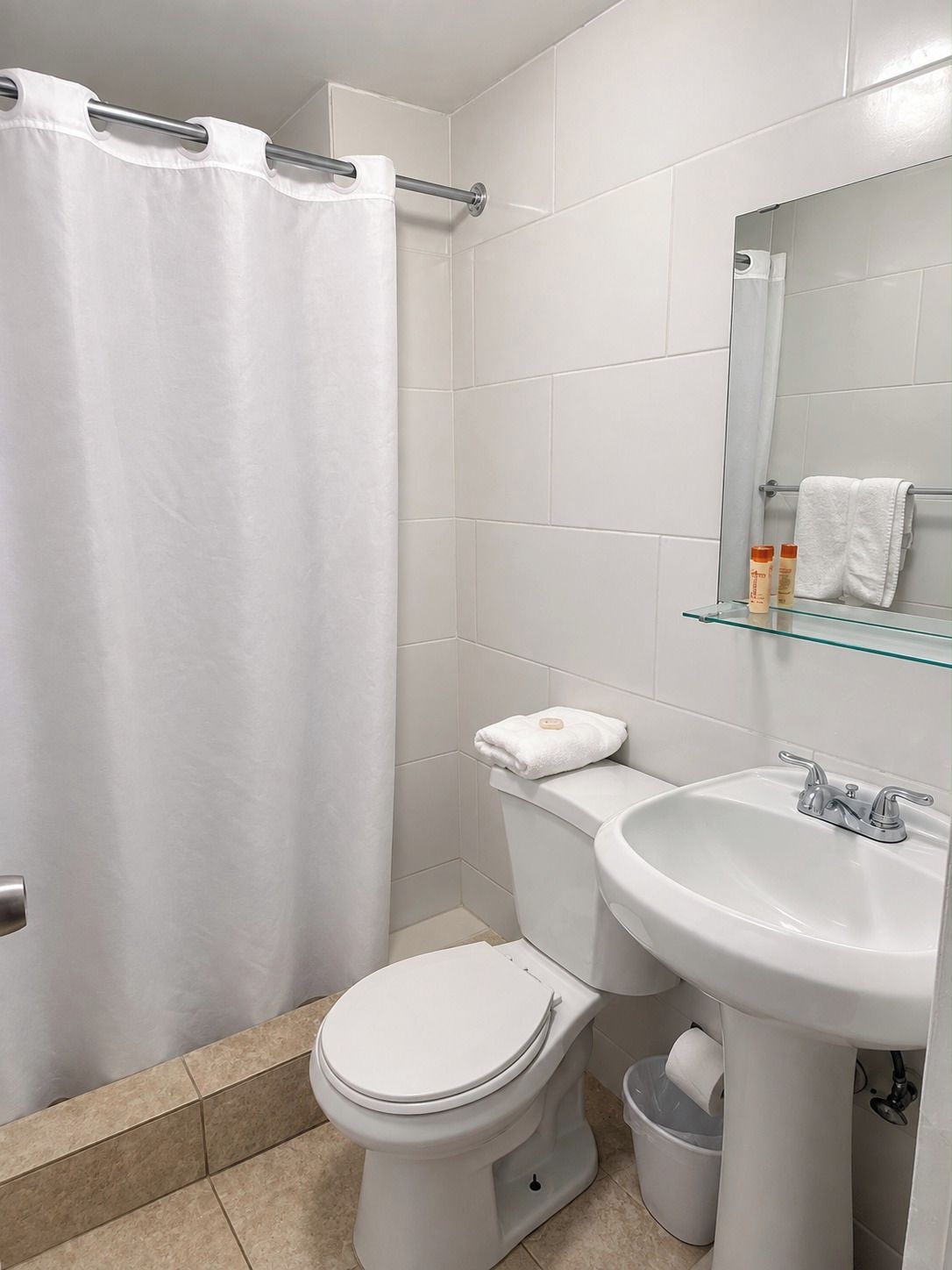 A bathroom with a white toilet, a glass shelf with toiletries, and a shower curtain.
