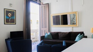 A room with a brown sofa, two blue chairs, a white table, a large mirror, and a framed picture on the wall. - Gladiolas 2202 (Ponce)