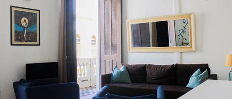 A room with a brown sofa, two blue chairs, a white table, a large mirror, and a framed picture on the wall.