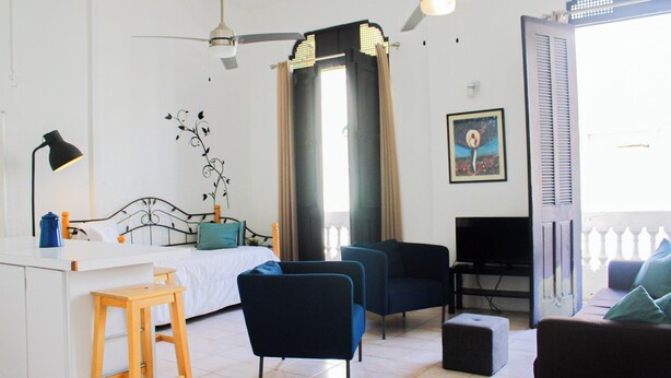 A bedroom with a bed, a desk, a chair, a TV, and a balcony with a railing. - Gladiolas 2202 (Ponce)