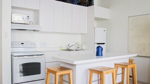 A modern kitchen with white cabinetry, a built-in oven, a microwave, a coffee maker, and two wooden stools. - Gladiolas 2202 (Ponce)