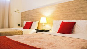 A hotel room with two beds, each with white bedding and red pillows, a nightstand with a lamp, and a wooden headboard. - Gladiolas 2202 (Ponce)