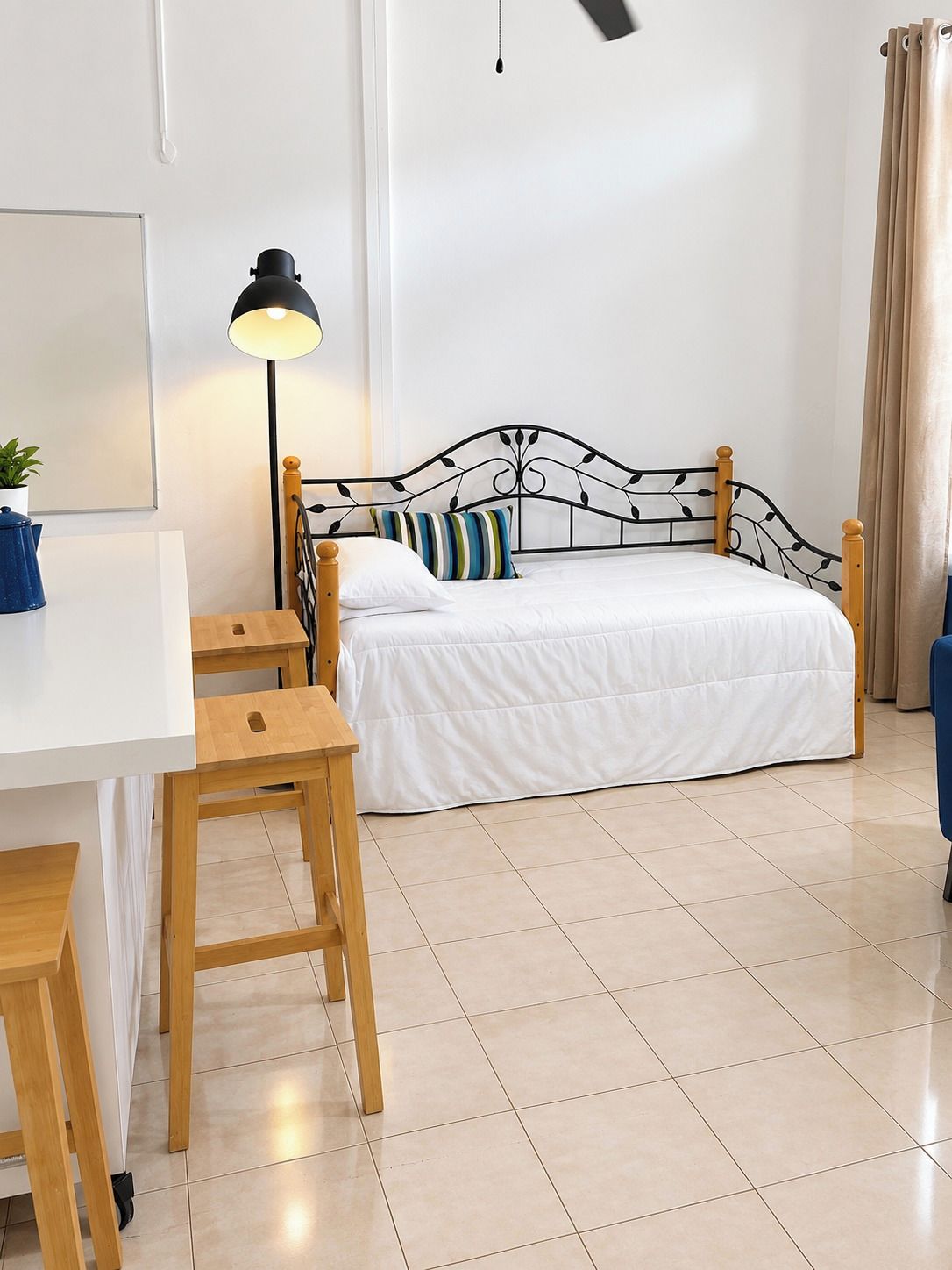 Un dormitorio con cama, escritorio, silla, lámpara y cortina.
