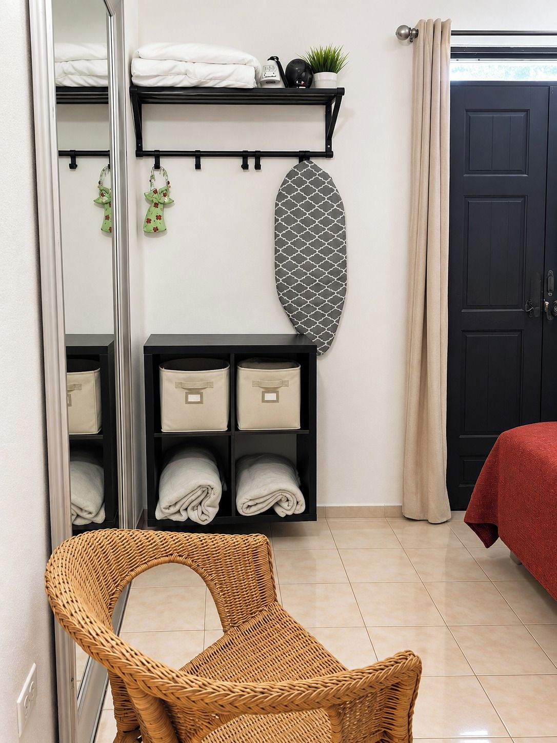 Un dormitorio con cama, armario, espejo, estante con toallas y una silla de mimbre.