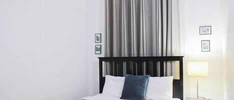 Een slaapkamer met een bed, nachtkastje, lamp en gordijnen.