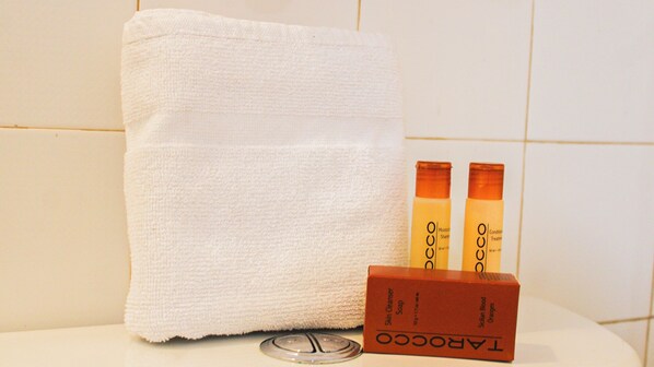 A white towel, two bottles of skin care products, and a soap bar on a white surface.