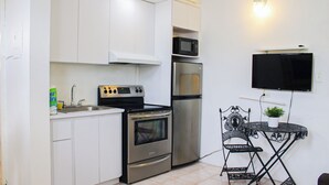 A compact kitchen with white cabinets, a stove, oven, microwave, and a refrigerator. There's a small table with a plant and a chair. - Gladiolas 2203 (Ponce)