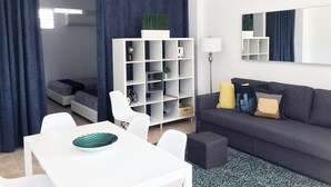 A modern living room with a dark grey sofa, white chairs, a white coffee table, and a bookshelf. - Boulevard 101 (Mayagüez)