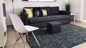 A modern living room with a grey sofa, a white chair, a black ottoman, and a black and white patterned rug. - Boulevard 101 (Mayagüez)