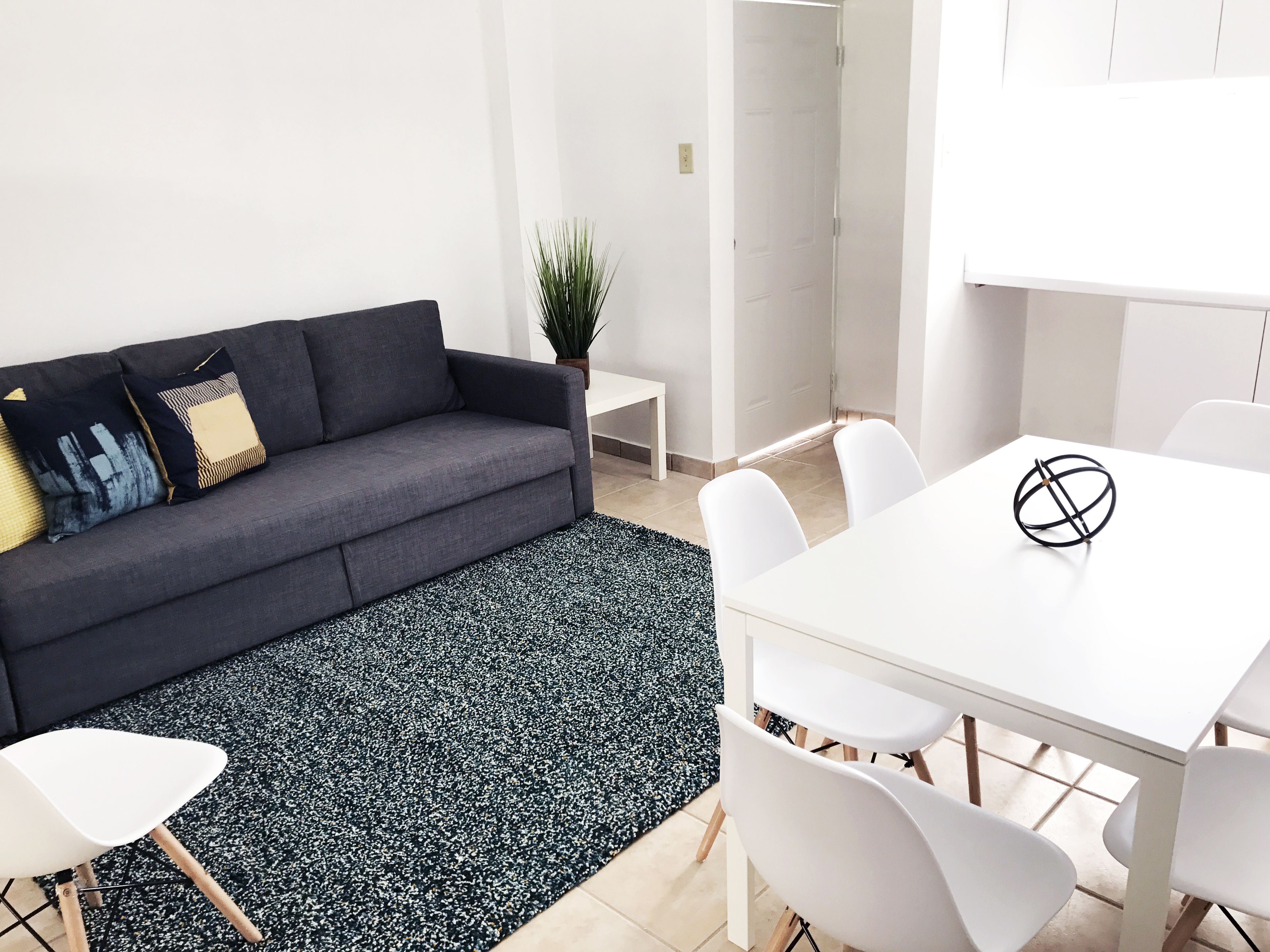 A modern living room with a dark grey sofa, white chairs, and a white table.