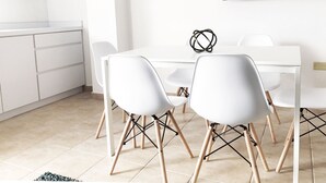 Una cocina moderna con armarios blancos y un microondas, una zona de comedor con una mesa y sillas blancas, y una pizarra en la pared.