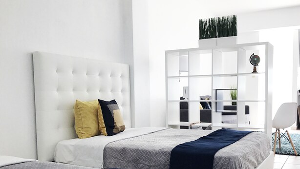 Un dormitorio moderno con dos camas, cabecera blanca y un ventanal grande.