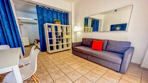 Un salon avec un canapé gris, un meuble TV blanc et un coin repas comprenant une table et des chaises.