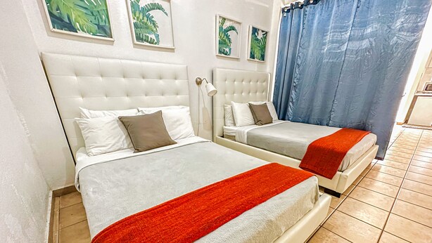 Une chambre d’hôtel avec deux lits, une tête de lit blanche, un plaid rouge et des œuvres d’art représentant des feuilles tropicales, encadrées et accrochées au mur.