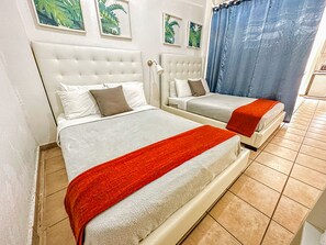 A hotel room with two beds, a white headboard, a red throw blanket, and framed tropical leaf artwork on the wall. - Boulevard 103 (Mayagüez)