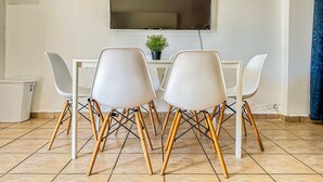 Un coin repas avec une table blanche, quatre chaises blanches et un téléviseur fixé au mur.