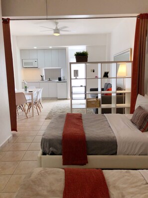 A modern bedroom with a bed, a bedside table, and a view into the kitchen area. - Boulevard 104 (Mayagüez)