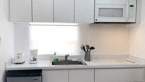 Ett kompakt kök med inbyggd diskmaskin, mikrovågsugn och diskho.