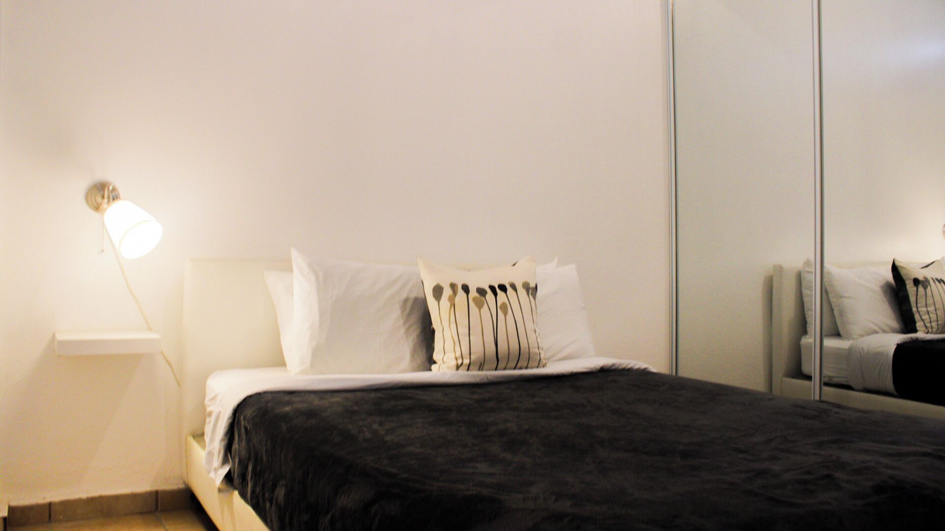 A neatly made bed with white and black bedding, a bedside lamp, and a mirror on the wall.