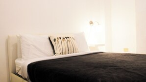 A bed with white and black bedding, a white pillow, and a bedside table with a lamp. - Boulevard 106 (Mayagüez)
