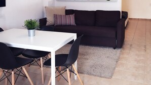 A modern living room with a white dining table, black chairs, a dark brown sofa, and a large mirror on the wall. - Boulevard 106 (Mayagüez)