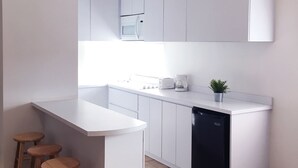 A modern kitchen with white cabinets, a built-in microwave, a coffee maker, and a dishwasher. There are wooden stools at the counter. - Boulevard 106 (Mayagüez)