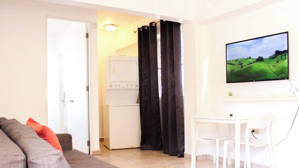 Un salon avec un canapé gris, une petite table et un téléviseur fixé au mur.