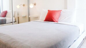 Un lit bien fait, avec des oreillers blancs et rouges, une table de chevet avec une lampe et un miroir qui reflète la pièce.