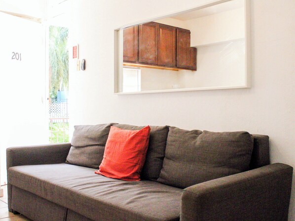 Un sofá gris con un cojín rojo, un armario de madera y una pared blanca.