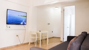 Un salon avec un téléviseur, une petite table avec deux chaises et un canapé.