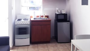 Une cuisine de taille réduite, équipée d’une cuisinière, d’un évier et d’un réfrigérateur, de placards en bois et d’un ventilateur de plafond.