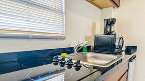 A kitchen with a black stove, a sink, a coffee maker, and wooden cabinets. - Boulevard 204 (Mayagüez)