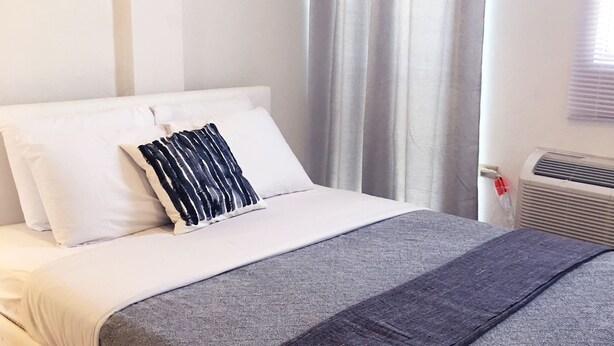 A neatly made bed with white and gray bedding, a dark gray blanket, and a striped pillow. - Boulevard 205 (Mayagüez)