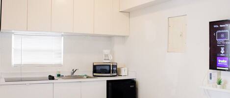 A small kitchenette with white cabinets, a microwave, a coffee maker, and a trash bin.