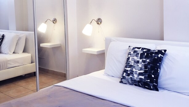 A modern bedroom with a bed, a nightstand, a mirror, and two wall-mounted lamps. - Boulevard 207 (Mayagüez)
