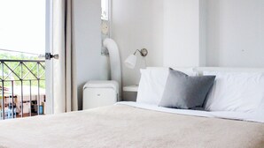 A bedroom with a bed, a nightstand, a lamp, and a window. - Boulevard 207 (Mayagüez)
