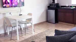 A modern living room with a flat-screen TV, a dining area with a white table and chairs, a kitchen with dark wooden cabinets, and a ceiling fan. - Boulevard 301 (Mayagüez)