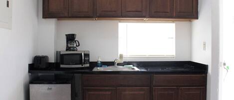 A kitchen with dark wooden cabinets, a stainless steel refrigerator, a microwave, a coffee maker, and a window providing natural light.
