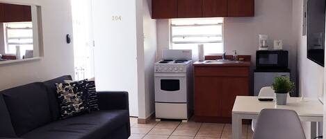 A compact living space with a kitchenette, a sofa, a dining table, and a TV.