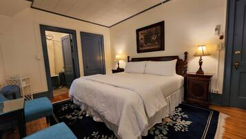 A bedroom with a large bed, two bedside lamps, a ceiling fan, a painting on the wall, and a door with a mirror.