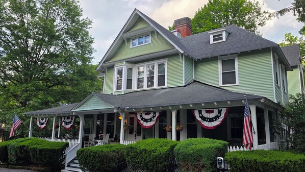 A green house with a porch, white picket fence, and American flags. - Vine Cottage Inn (Hot Springs)
