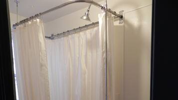 A bathroom with a freestanding bathtub, a shower curtain, and a showerhead.