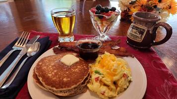 A breakfast plate with pancakes, scrambled eggs, bacon, and a glass of beer.